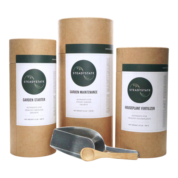 Three paper tubes with garden starter, garden maintenance, and houseplant fertilizers with an aluminum metal scoop and bamboo spoon.